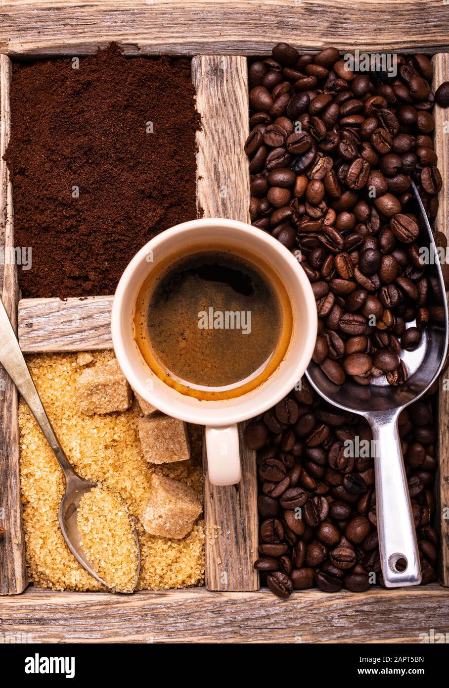 Im rustikalen Holzbehälter mit Draufsicht, einer Tasse Espresso, rohem Rohrzucker und geröstetem Kaffee. Stockfoto