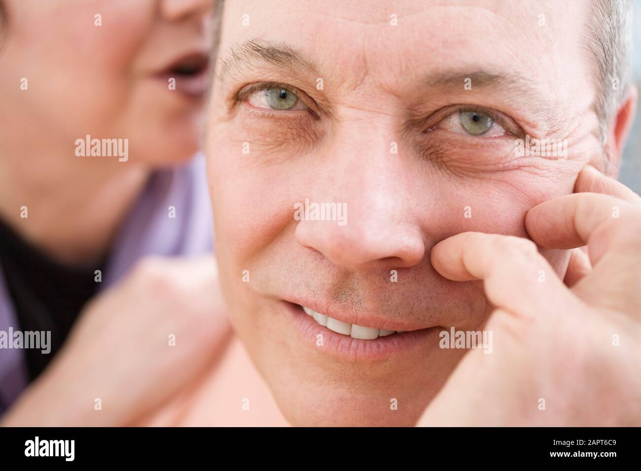 Porträt eines reifen Mannes mit Frau, die ihm ins Ohr flüstert. Stockfoto