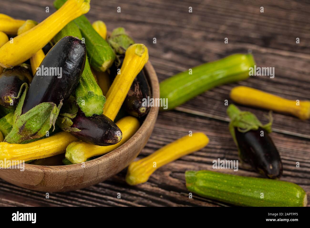 Baby-Aubergini und Zucchini in Bambusschale auf Holztischhintergrund Stockfoto