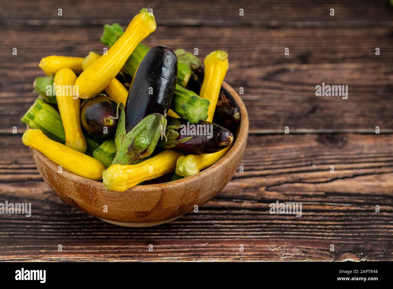 Baby-Aubergini und Zucchini in Bambusschale auf Holztischhintergrund Stockfoto