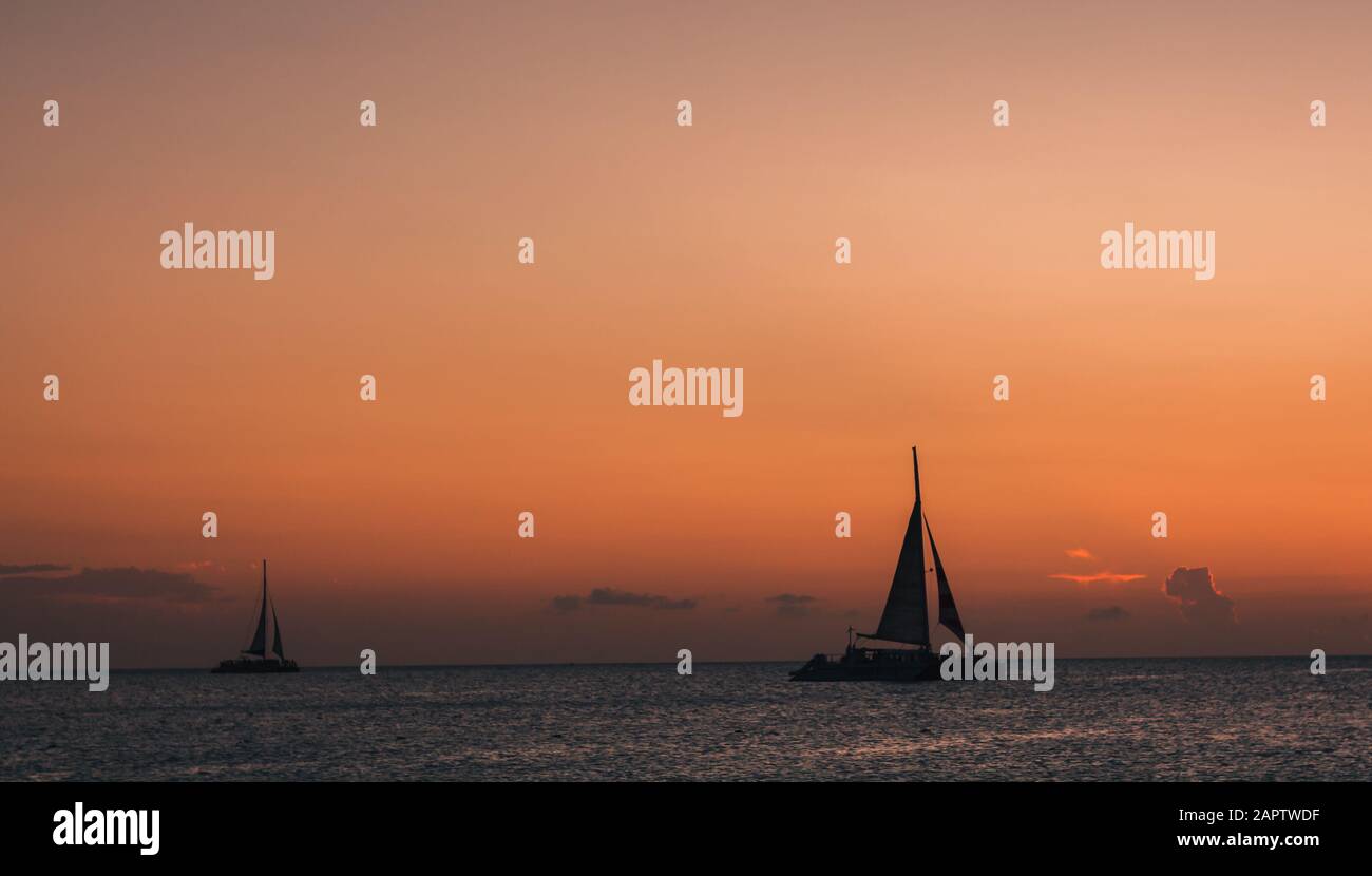 Eagle Beach, Aruba. Genießen Sie den Sonnenuntergang, während Segelboote am Horizont des Sonnenuntergangs vorbeifahren. Stockfoto