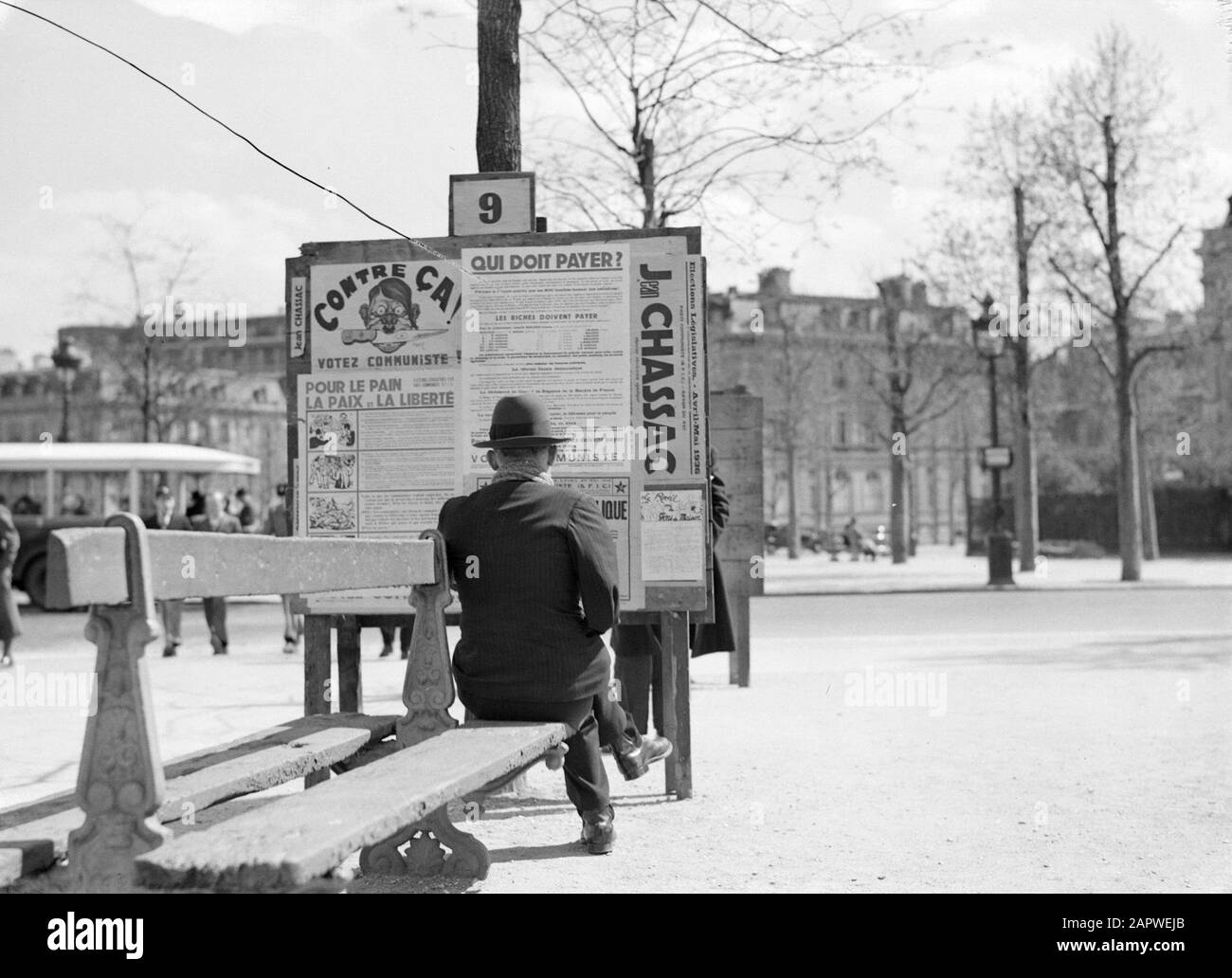 Mann auf der Couch in Paris schaut auf Schild mit Wahlplakaten der französischen Parti Communiste, mit Jean Chassac als Kandidat für das parlament Anmerkung: Oben links auf der Plakatwand eine Karikatur von Adolf Hitler Datum: 1936 Ort: Frankreich, Paris Schlüsselwörter: Plakate, Kommunismus, Straßenbilder, Wahlen, Wahlkampagnen, Bänke persönlicher Name: Chassac, Jean, Hitler, Adolf Stockfoto