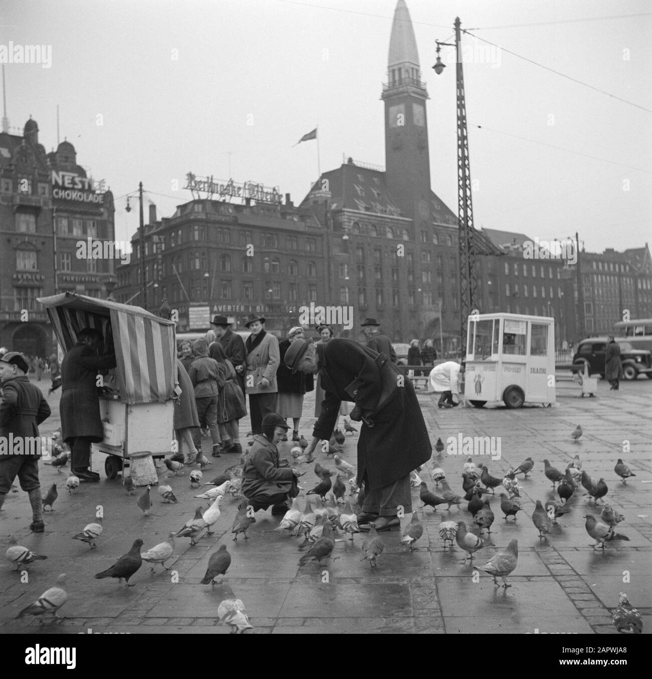 Der Rathausplatz in Kopenhagen Steht Für einen Stall, in dem Taubenfutter verkauft wird, im Vordergrund ein Mann und Kind, das Tauben füttert, und im Hintergrund das Rathaus von Kopenhagen Datum: März 1954 Standort: Dänemark, Kopenhagen, Rådhuspladsen Schlüsselwörter: Plakate, Tauben, Lebensmittel, Gebäude, Rathäuser, Kinder, Kioske, Werbung, Straßenbilder, Türme, Lebensmittel, Futter, Fußgänger Stockfoto