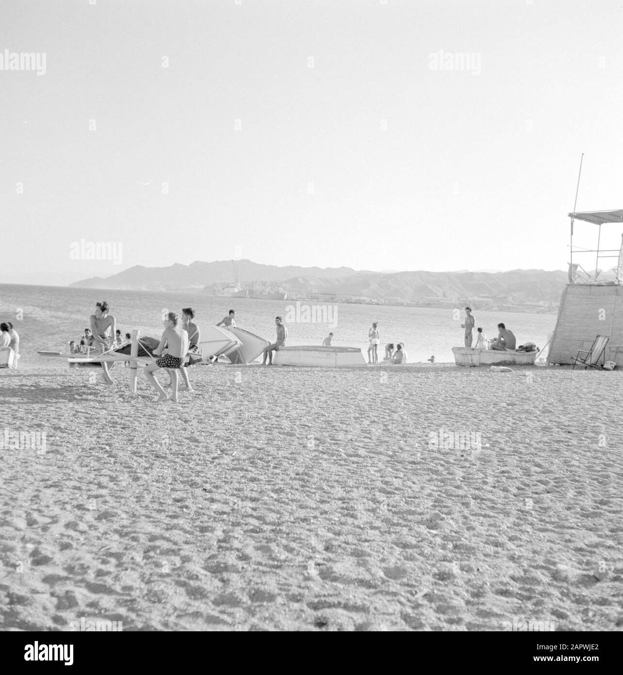 Menschen am Strand in der Nähe von Eilat mit Blick auf den Golf von Akaba und den Hafen von Eilat. Genau ein Blick auf den Rettungsschwimmer Datum: 1. Januar 1963 Ort: Eilat, Golf von Aqaba, Israel Schlüsselwörter: Rettungsschwimmer, Rettungsschwimmer, Berge, Häfen, Strände Stockfoto