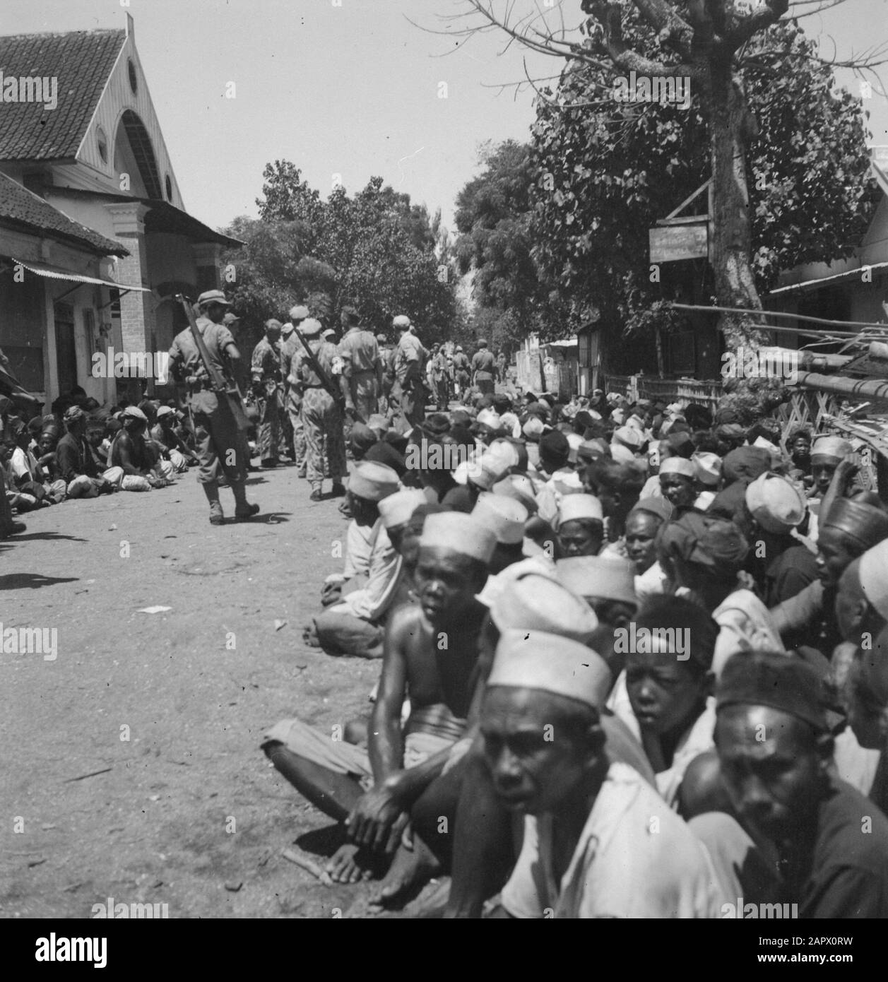 Die kontemplatierende Lektion Pasuruan Pasaroean: Bereichert von religiösen Lehrern, die von der Regierung von Djocja angewiesen wurden, verübten die Leute von kampong Lokok ein brutales Massaker unter den chinesischen Einwohnern. Beim unerwarteten Erscheinen der holländischen Patrouille verschlagen die Massen, die bei der schrecklichen Ermordung von 26 Chinesen halfen, in verängstigter Unsicherheit, während Soldaten die Orte aufspüren, an denen die verstümmelten Leichen versteckt sind Datum: August 1947 Ort: Indonesien, Niederländisch-Indien Stockfoto