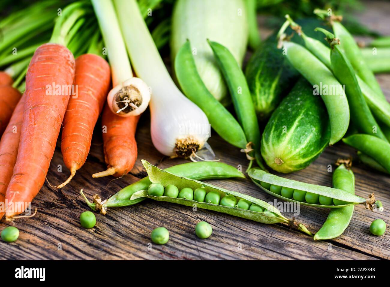 Verschiedene frische Gemüsesorten. Erbsen, Karotten, Gurken, Zucchini und Zwiebeln auf einem Holztisch, gesunde Nahrung. Selektiver Fokus. Stockfoto