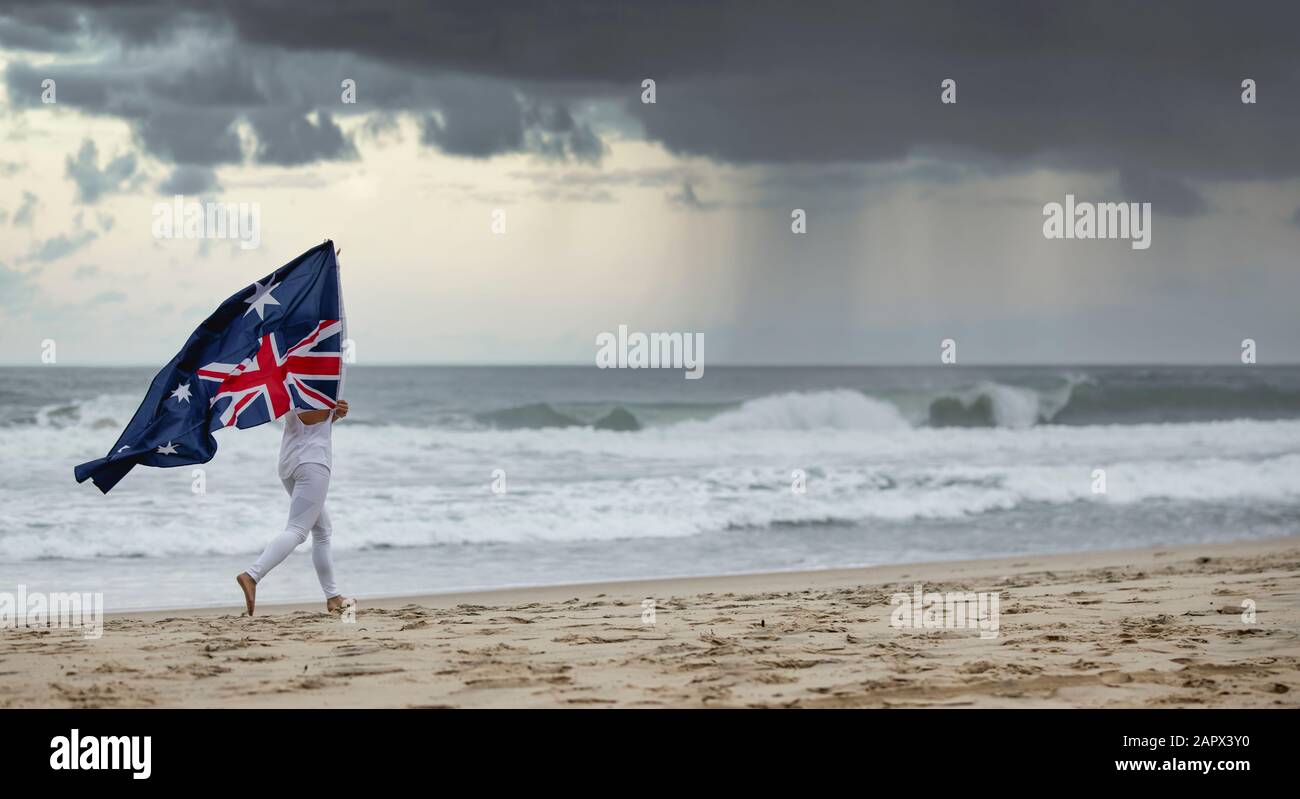 Australische Flagge, die im Wind weht und von einer Frau beim Joggen an einem australischen Strand gehalten wird, Stockfoto