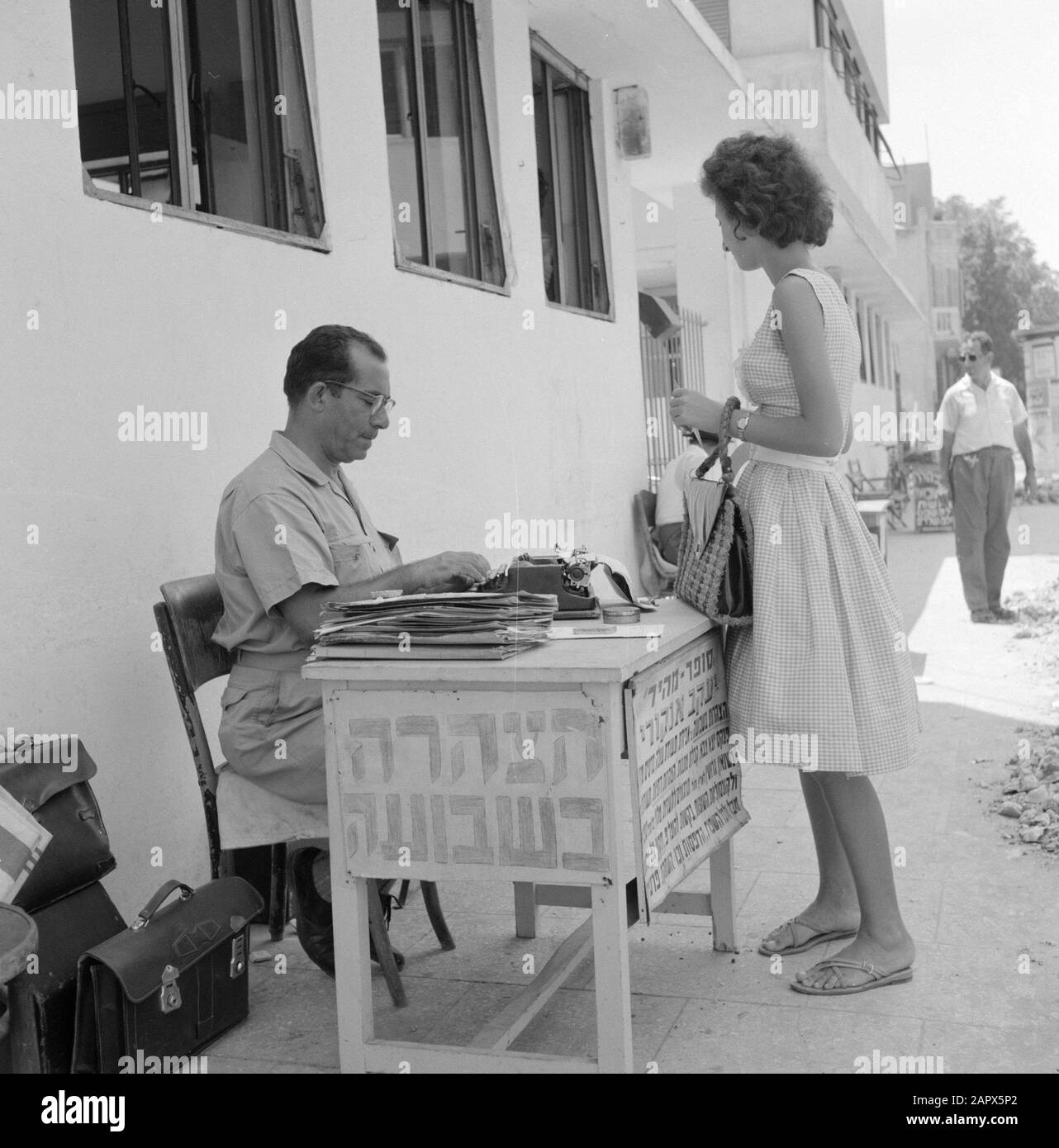 Israel 1964-1965: Tel Aviv, öffentliche Schriftsteller öffentliche Autoren öffentliche Autoren sitzen mit einer Schreibmaschine hinter einem Tisch auf dem Bürgersteig und bieten ihre Dienste den Passanten in Annotation an: Die neuen Einwohner Israels kämpfen nach ihrer Einwanderung lange mit der Sprache. Öffentliche Autoren, die vor offiziellen Büros sitzen, sind Immigranten beim Schreiben von Briefen/Anfragen usw. behilflich Datum: 1964 Ort: Israel, Tel Aviv Schlüsselwörter: Schreibmaschinen, Schriftsteller, Straßenstatuen, Fußgänger, Fußwege Stockfoto