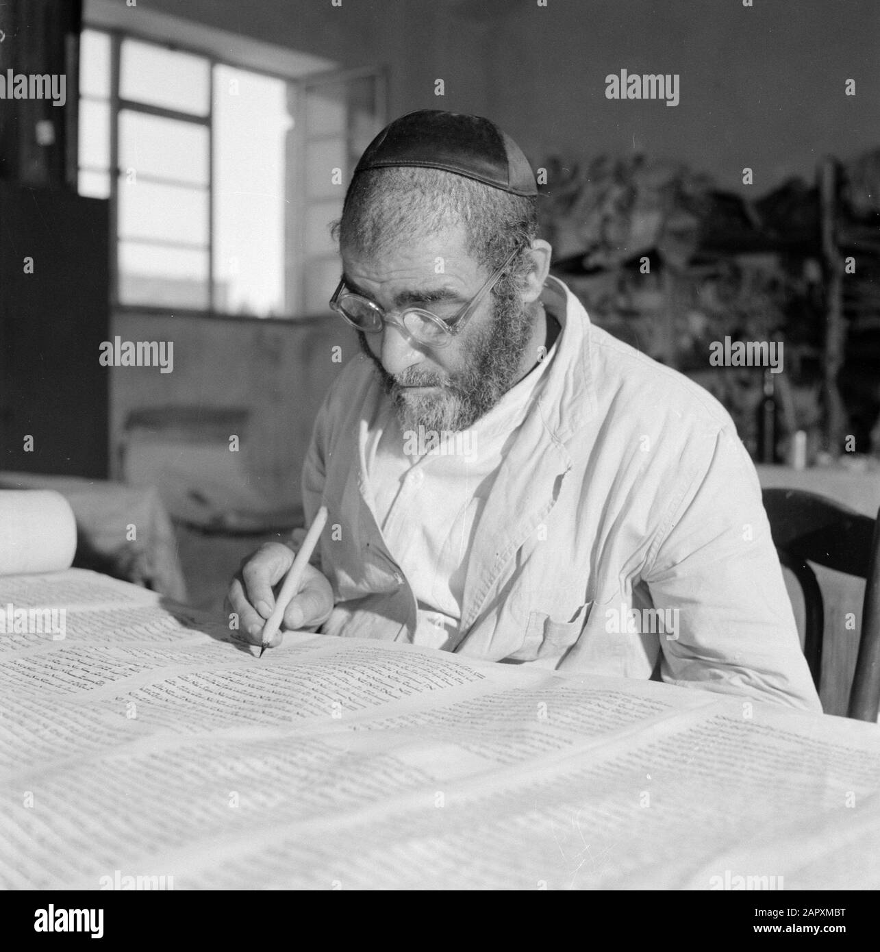 Israel 1964-1965: Jerusalem (Jerusalem), Thorarrolls Torah Writer at Work hinter einem Arbeitstisch Anmerkung: Die Tora (das Mosaische Gesetz) ist auf einer Rolle geschrieben, die aus Pergament von der Haut eines koscheren Tieres besteht. Die verschiedenen Teile von Pergament sind mit einer Sehne aneinander befestigt, der Text wird handschriftlich geschrieben. Die Tinte wird oft von selbst hergestellt und muss bestimmte Anforderungen erfüllen. Schließlich ist die Rolle an zwei Holzstöcken mit Griffen befestigt und beide Enden werden gegen das mittlere Datum gerollt: 1964 Ort: Israel, Jerusalem Schlüsselwörter: Tora, Handschrift, jüdische Religion, Schriftsteller, Arbeit Stockfoto