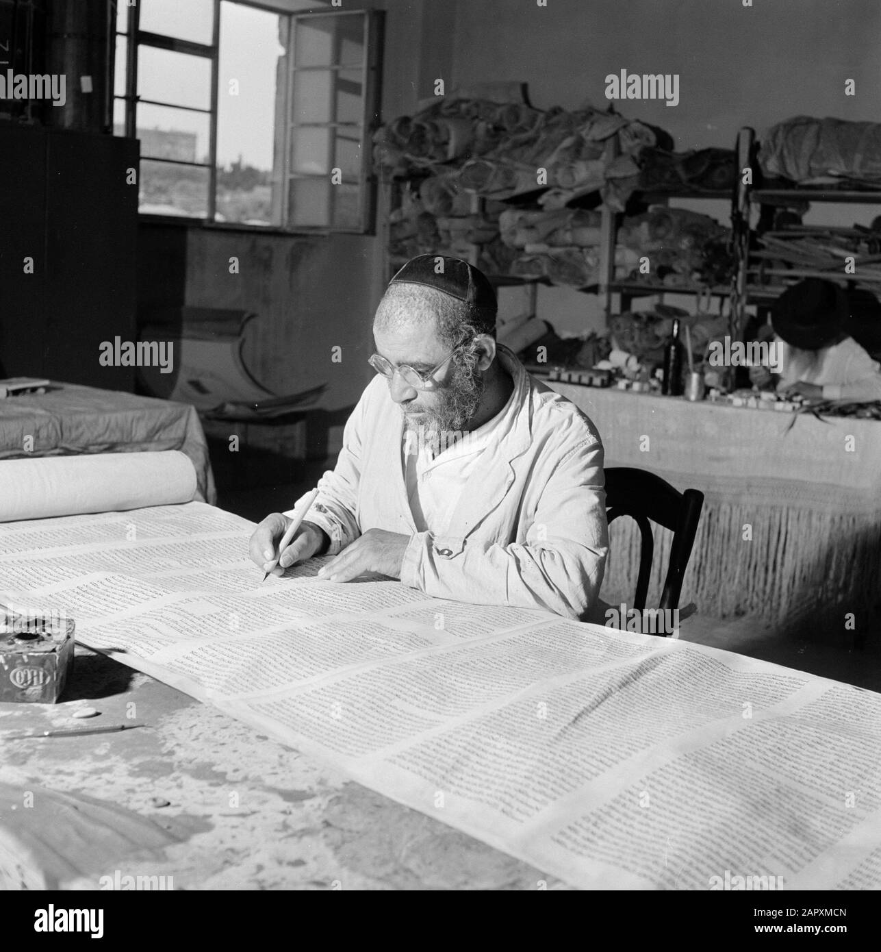Israel 1964-1965: Jerusalem (Jerusalem), Thorarrolls Torah Writer at Work hinter einem Arbeitstisch Anmerkung: Die Tora (das Mosaische Gesetz) ist auf einer Rolle geschrieben, die aus Pergament von der Haut eines koscheren Tieres besteht. Die verschiedenen Teile von Pergament sind mit einer Sehne aneinander befestigt, der Text wird handschriftlich geschrieben. Die Tinte wird oft von selbst hergestellt und muss bestimmte Anforderungen erfüllen. Schließlich ist die Rolle an zwei Holzstöcken mit Griffen befestigt und beide Enden werden gegen das mittlere Datum gerollt: 1964 Ort: Israel, Jerusalem Schlüsselwörter: Tora, Handschrift, jüdische Religion, Schriftsteller, Arbeit Stockfoto