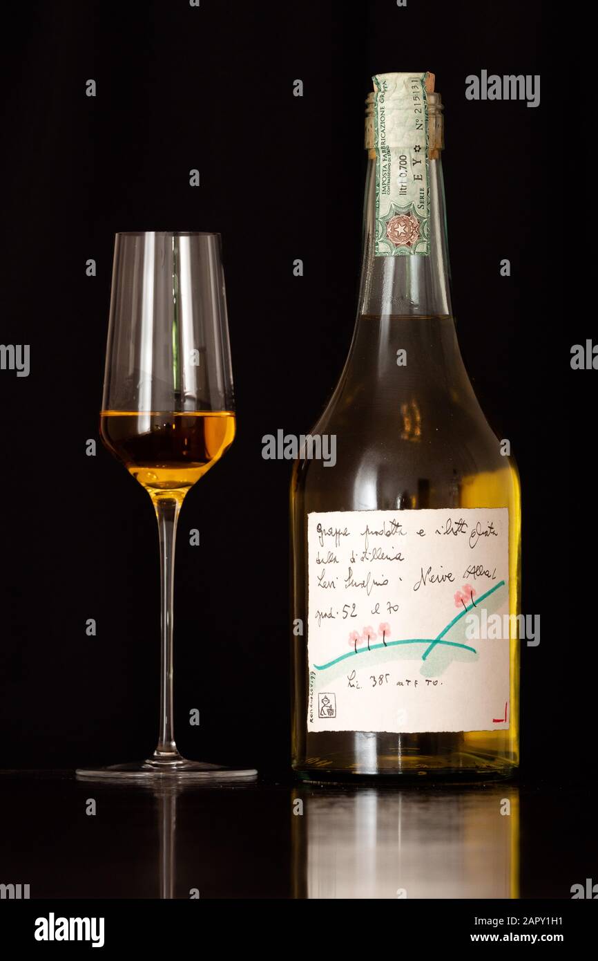 Neive, Alba, Italien - 12. Januar 2020: Originale Romano Levi Grappa Flasche mit Zeichnung aus dem Jahr 1995 mit einem Spirituosenglas auf dunklem Hintergrund. Stockfoto