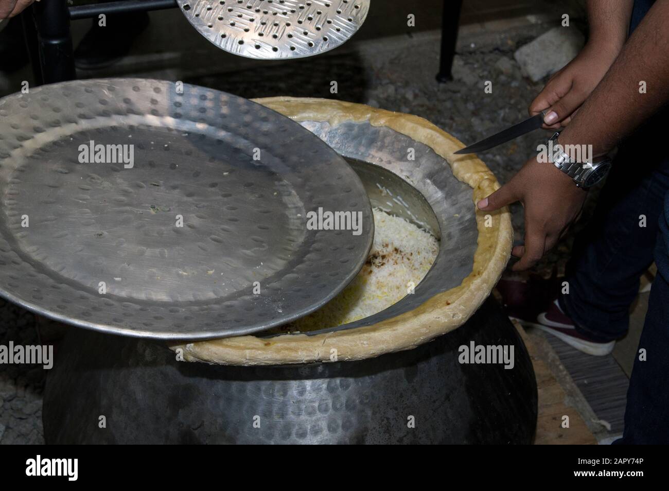 Die Hände des Küchenchefs schneiden Brot um einen Biriyani-Topf aus Aluminium, der traditionell zum Kochen von Reis verwendet wird. Dieses Gericht ist besonders in Hyderabad, Indien, verbreitet Stockfoto