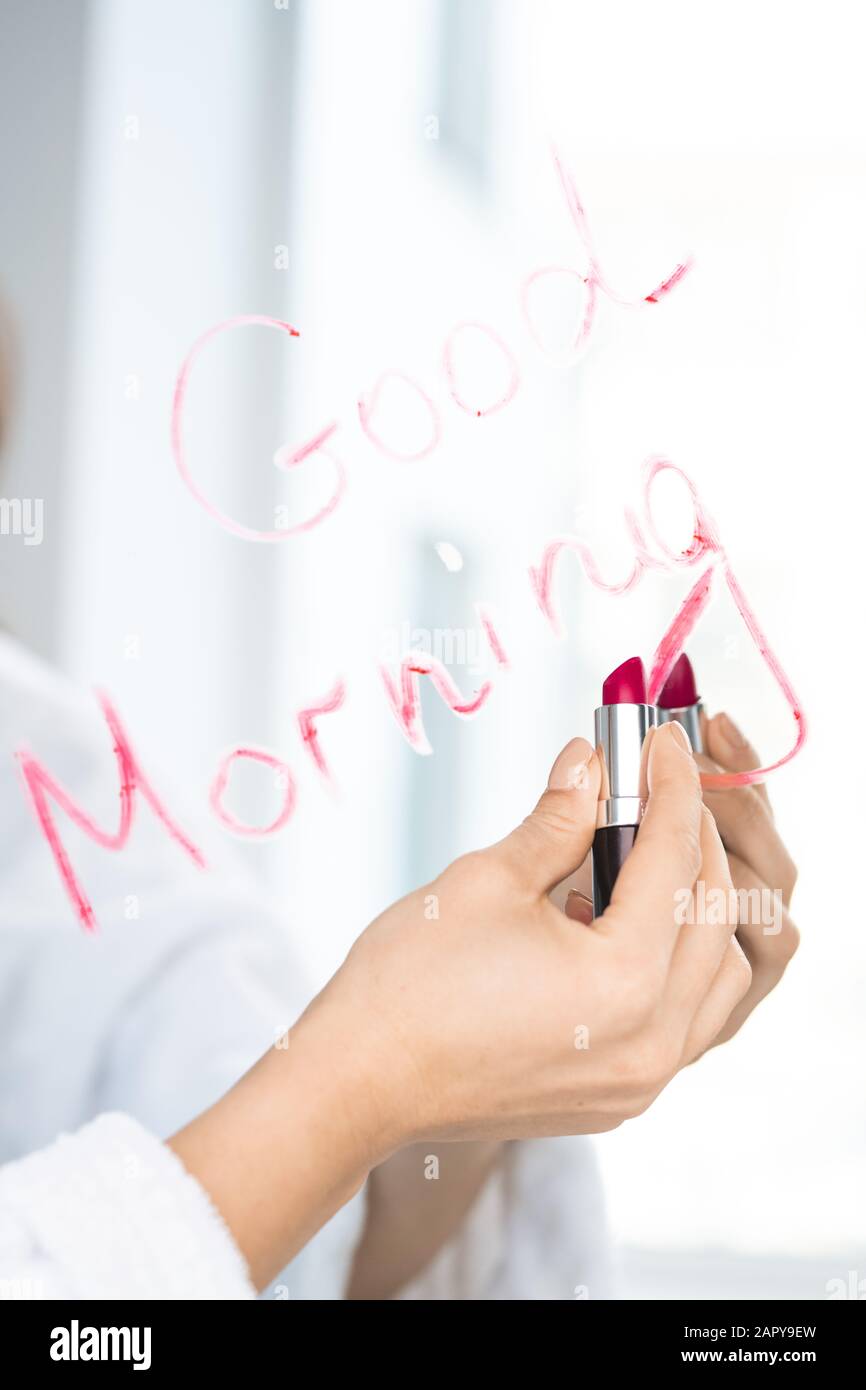 Hand der jungen Frau, die den Lippenstift der Farbe der Karmson in der Nähe des Spiegels hält Stockfoto