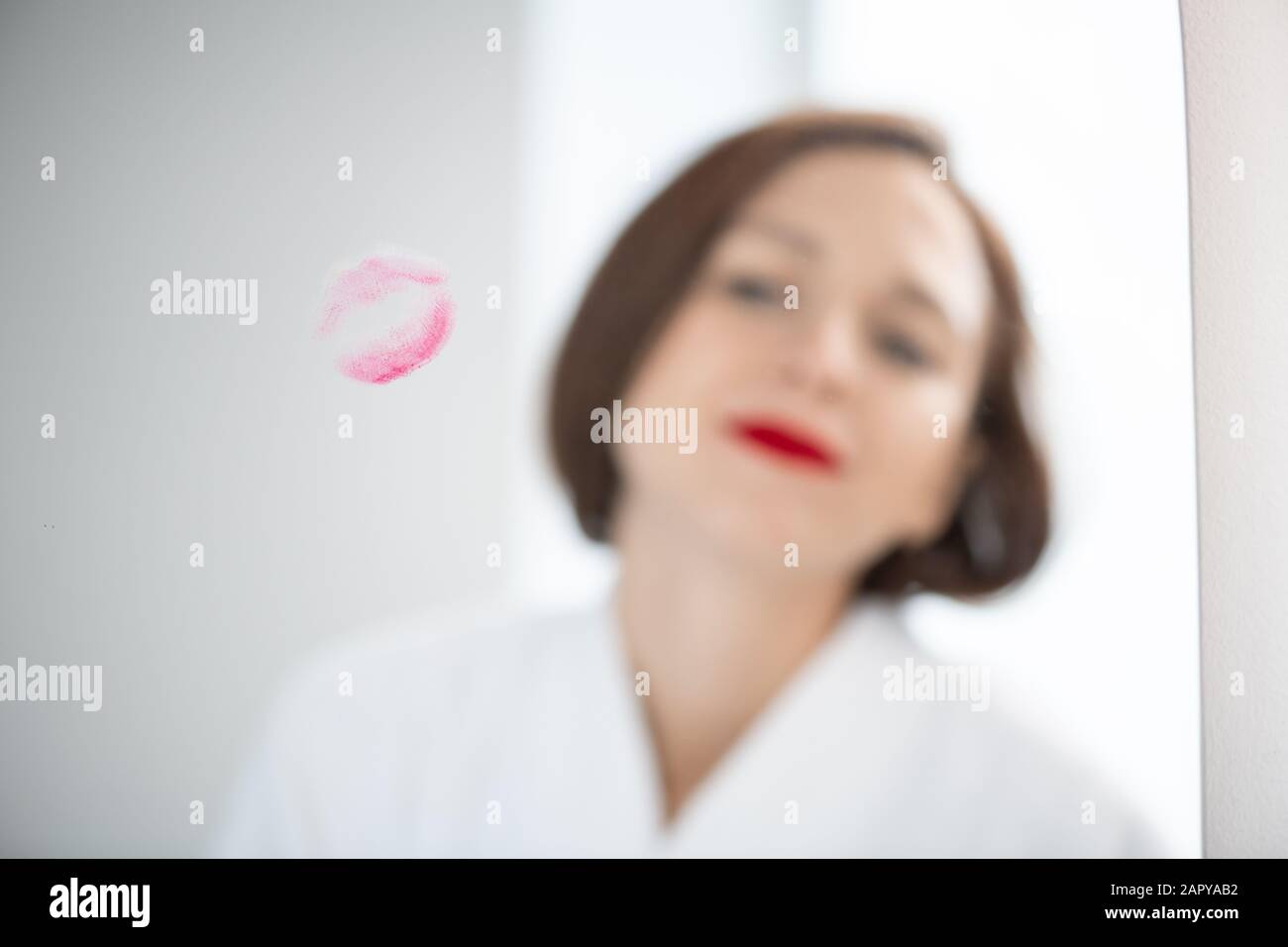 Spiegelung der jungen Frau im weißen bademantel, der vor dem Spiegel steht Stockfoto