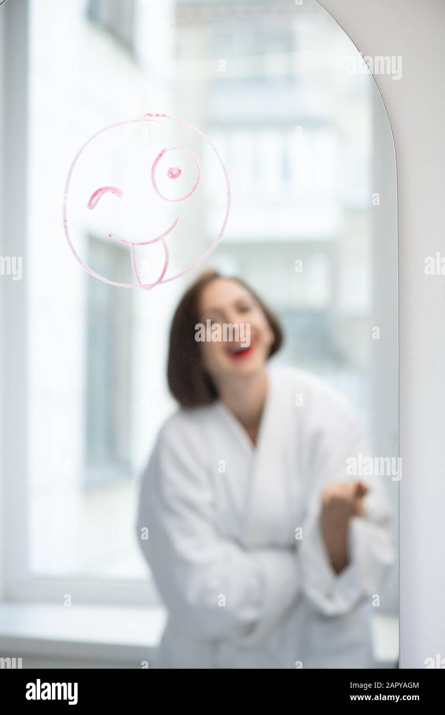 Lachendes Mädchen, das vor dem Spiegel steht, mit lustigem Gesicht, das mit Lippenstift gezeichnet wurde Stockfoto