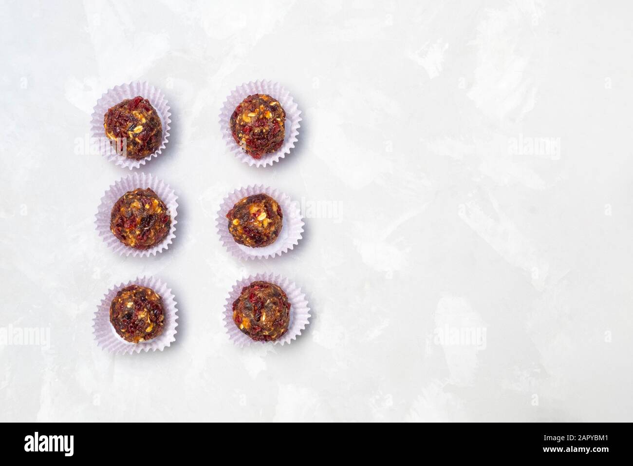 Hausgemachte Energiekugeln mit getrockneten Datteln, Preiselbeeren, Walnüssen, Hafer auf neutralem Betonhintergrund Stockfoto