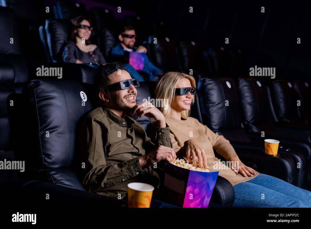 Junges lächelndes Paar in 3D-Brillen, das Zeit vor dem großen Bildschirm genießt Stockfoto