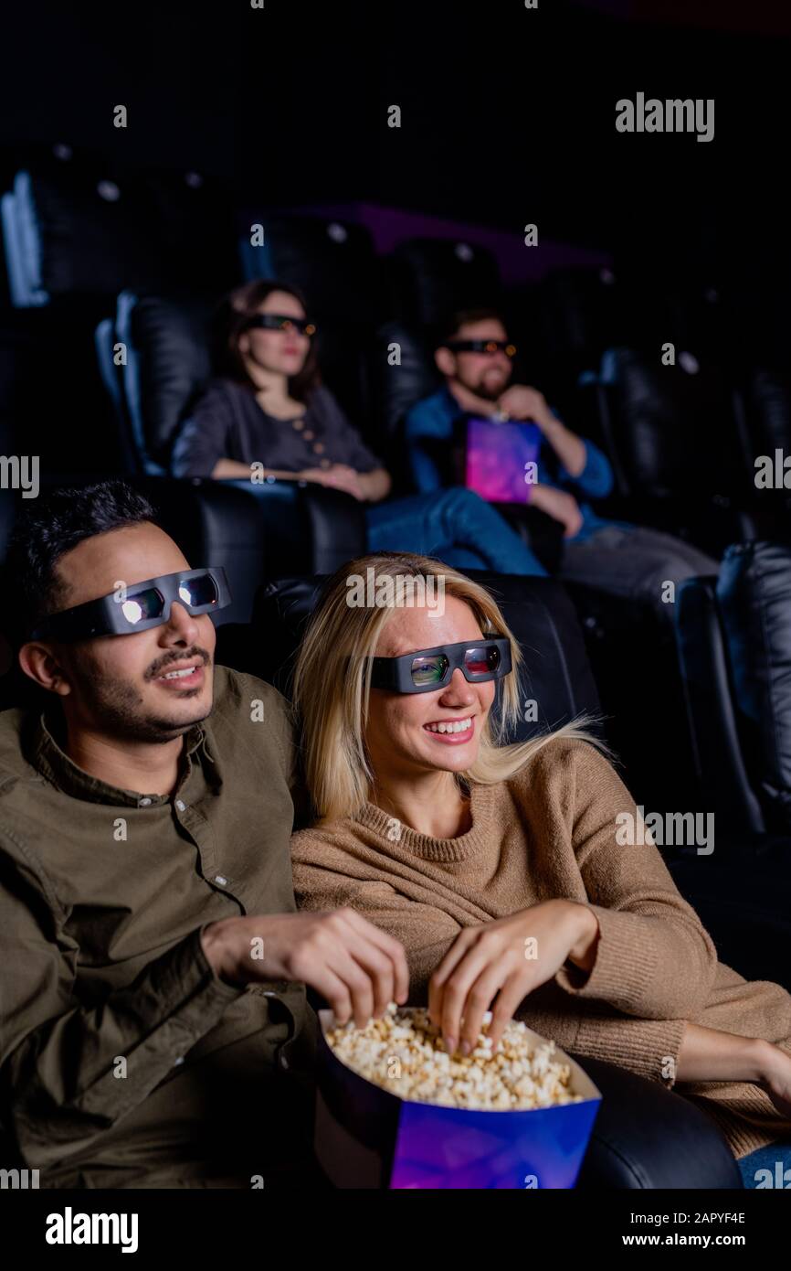 Fröhliche Daten in 3D-Brillen, die Popcorn essen, während sie vor dem Bildschirm sitzen Stockfoto