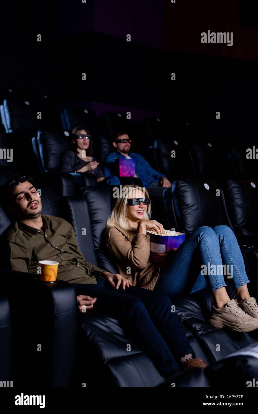 Müde, im Kino im Sessel schlafend, während seine Freundin den Film genießt Stockfoto