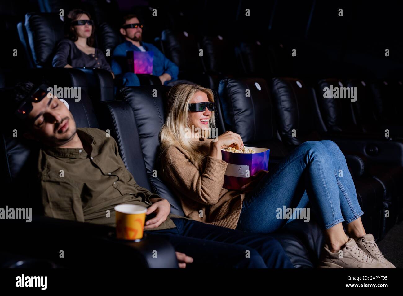 Junger, müder Mann schläft im Kino, während seine Freundin Film im Kino sieht Stockfoto