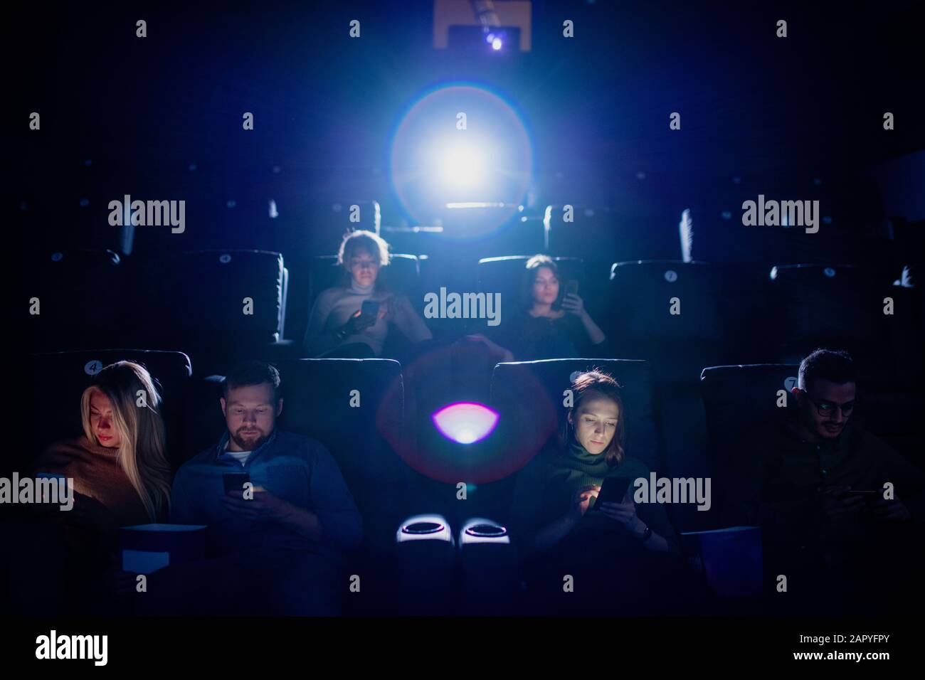 Eine Gruppe mobiler Jugendlicher scrollt im dunklen Kino in ihren Smartphones Stockfoto
