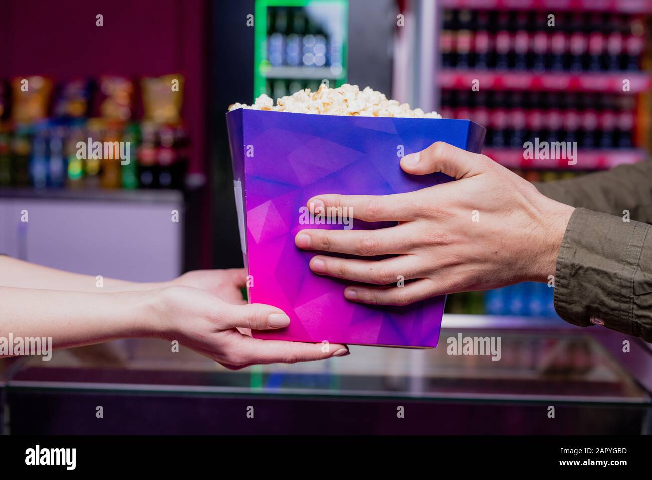 Hände des jungen Mannes, der eine große lila Papierbox voller Popcorn im Kino nimmt Stockfoto