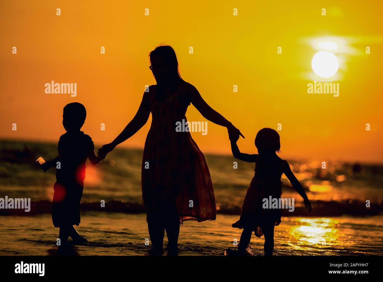Mutter und Kinder gehen bei Sonnenuntergang an einem Strand entlang Stockfoto