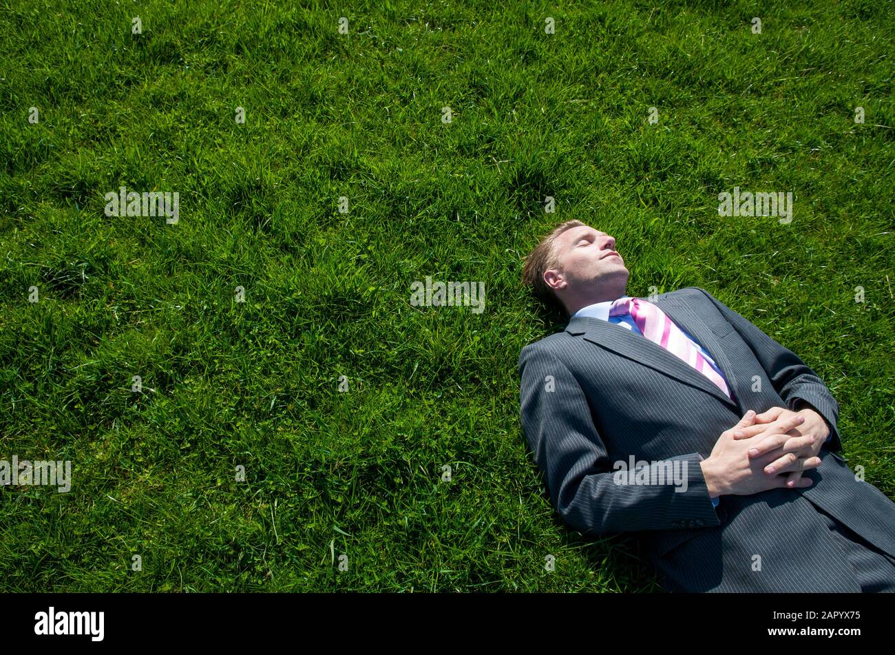 Entspannter Geschäftsmann, der an einem sonnigen Frühlingstag auf einem hellen grünen Rasenplatz liegt Stockfoto