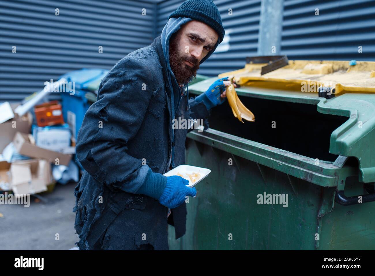 Bärtiger Bettler, der Lebensmittel in Trashcan sucht Stockfoto