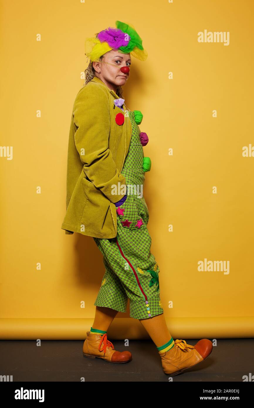Darstellerin mit farbenfrohem Clownkostüm auf hellgelbem Hintergrund Stockfoto