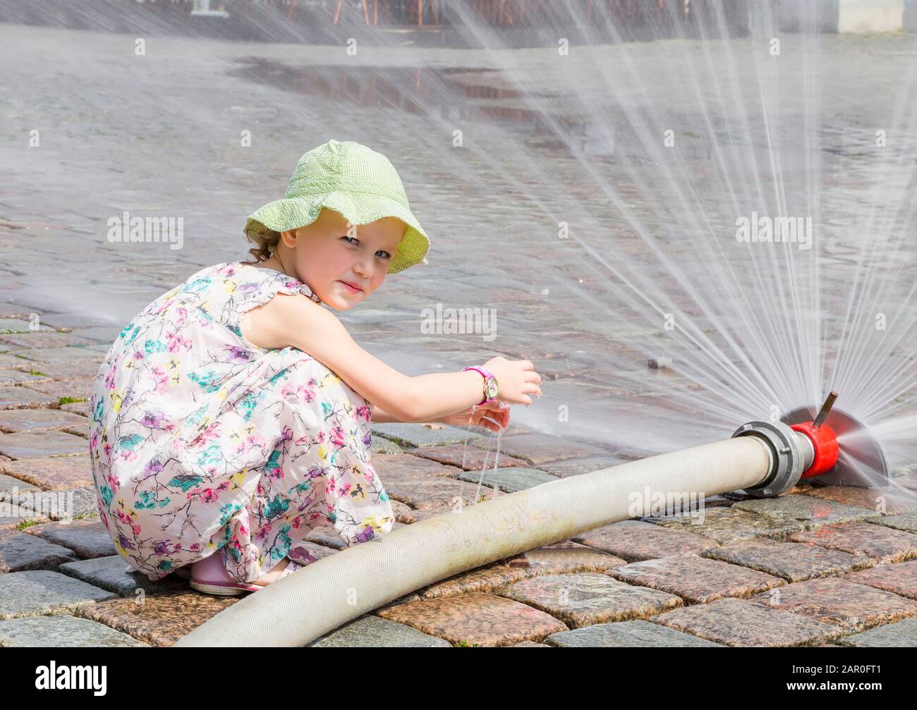 Ein kleines Mädchen spielt an einem heißen Sommertag mit einem Wasserstrahl aus einem Schlauch Stockfoto