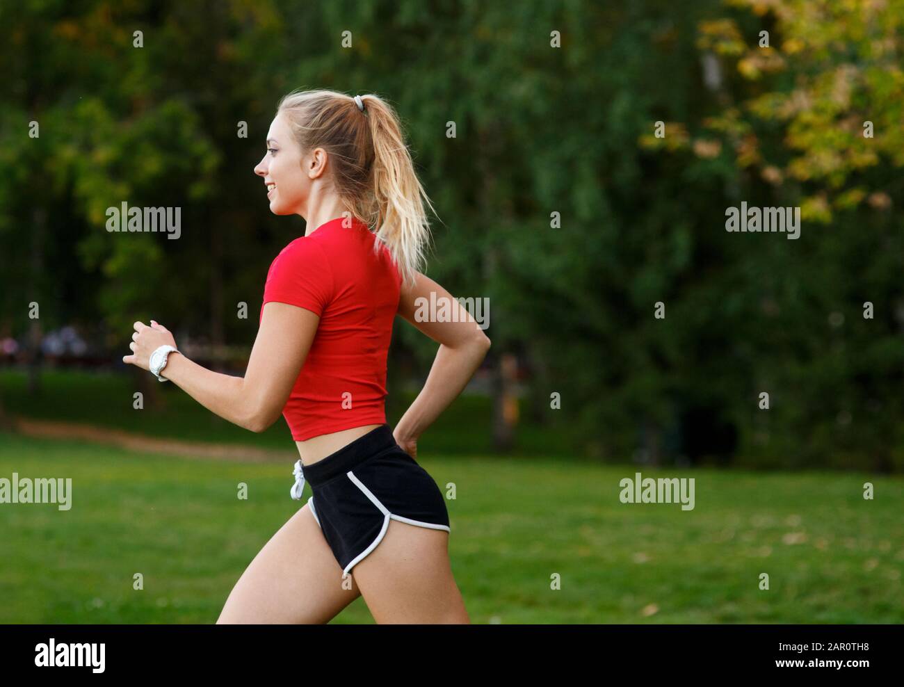 Ein junges Mädchen macht Sport im Freien, eine Frau in Shorts und ein rotes T-Shirt läuft in der Natur. Stockfoto
