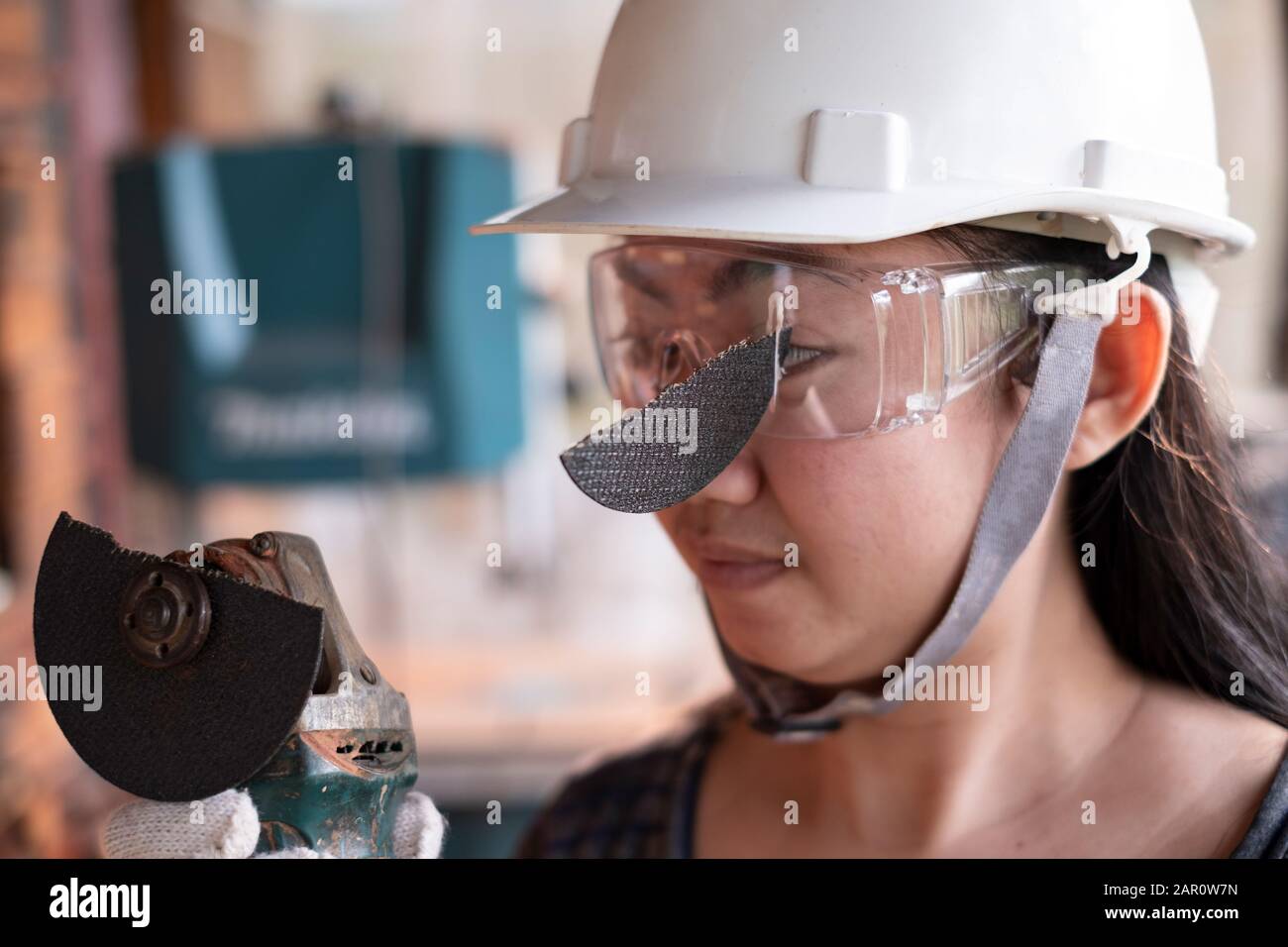 Tragen Sie eine Schutzbrille, damit diese Ingenieurin bei der Arbeit im Auge ist, da die Trennscheibe defekt ist, Gefahren durch die Verwendung von Werkzeugen, Sicherheit zuerst Stockfoto