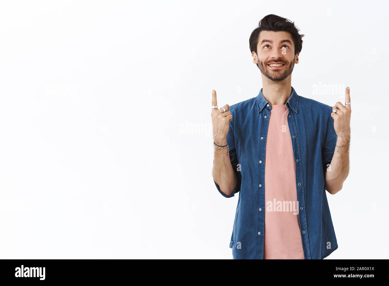 Fröhlicher schwuler Mann mit Bart, Frisur des Hüpfers, Schmuck, modernes Outfit, amüsant aussehend und aufgerichtet, lächelnd glücklich, checkend Stockfoto