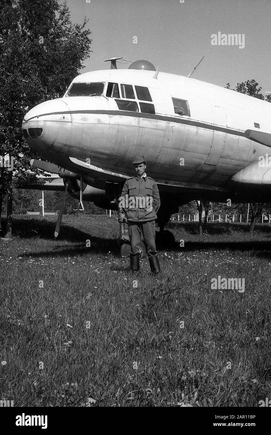 STUPINO, REGION MOSKAU, RUSSLAND - CIRCA 1992: Ein Soldat der russischen Armee vor dem Hintergrund eines sowjetischen zweimotorigen militärischen Frachttransportflugzeugs Iljuschin Il-14. Schwarz und Weiß. Filmscan. Große Körnung. Stockfoto