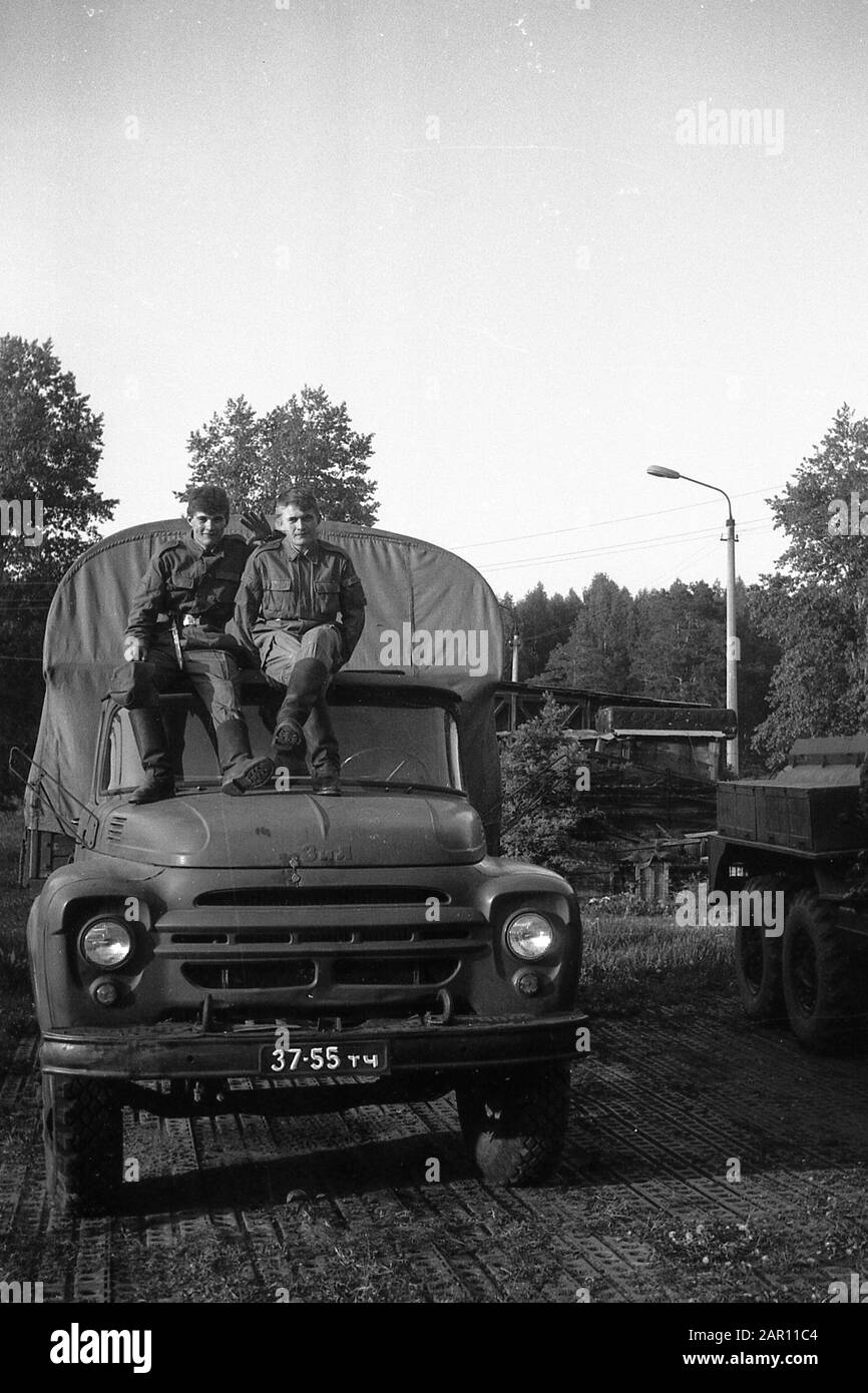 STUPINO, REGION MOSKAU, RUSSLAND - CIRCA 1992: Das Porträt zweier Soldaten der russischen Armee, die auf dem Kabinendach eines Lastwagens ZIL-130 sitzen. Schwarz und Weiß. Filmscan. Große Körnung. Stockfoto