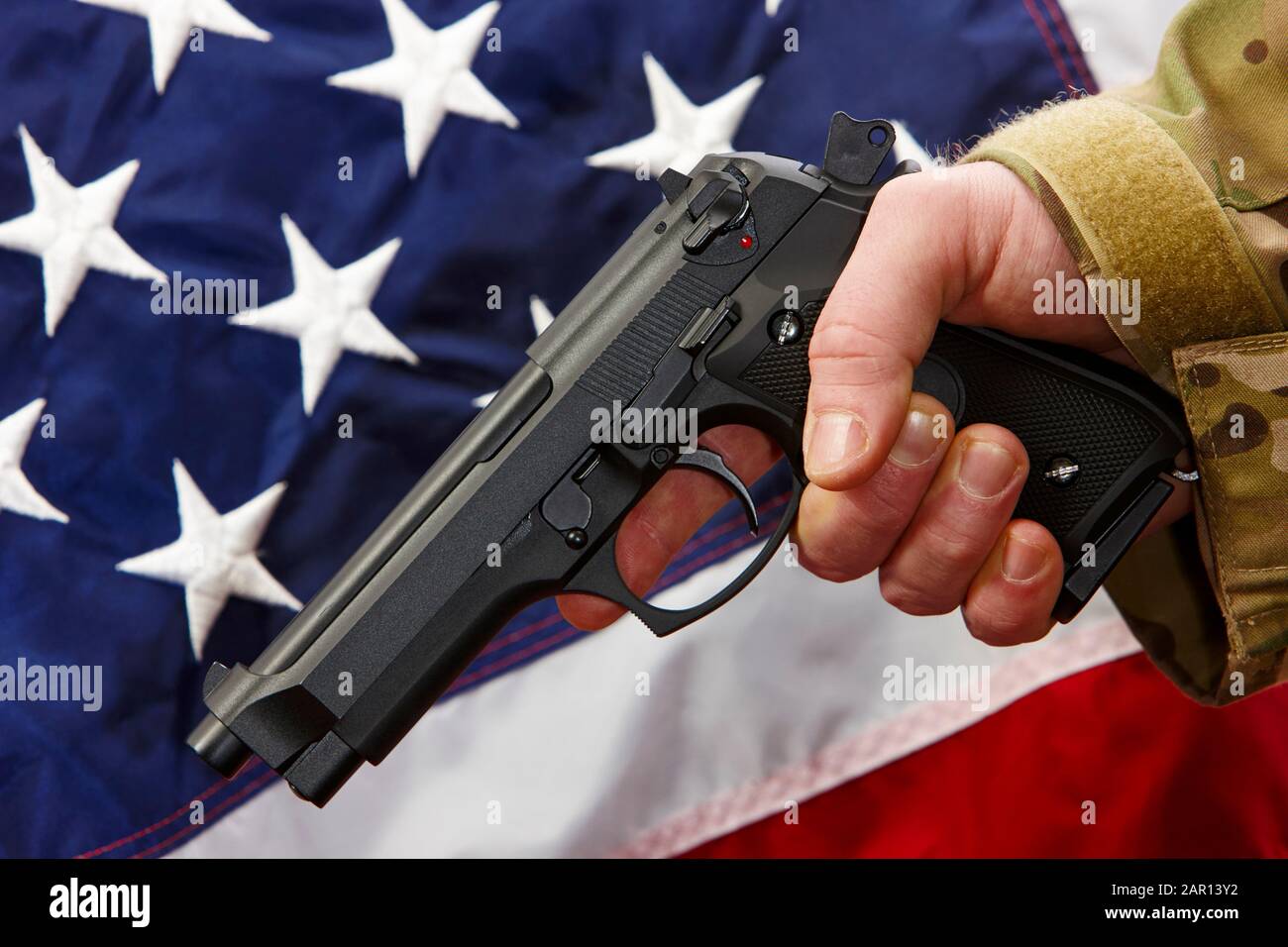 Mann in Strapazen holding Beretta Pistole vor Vereinigte Staaten von Amerika Flagge Stockfoto