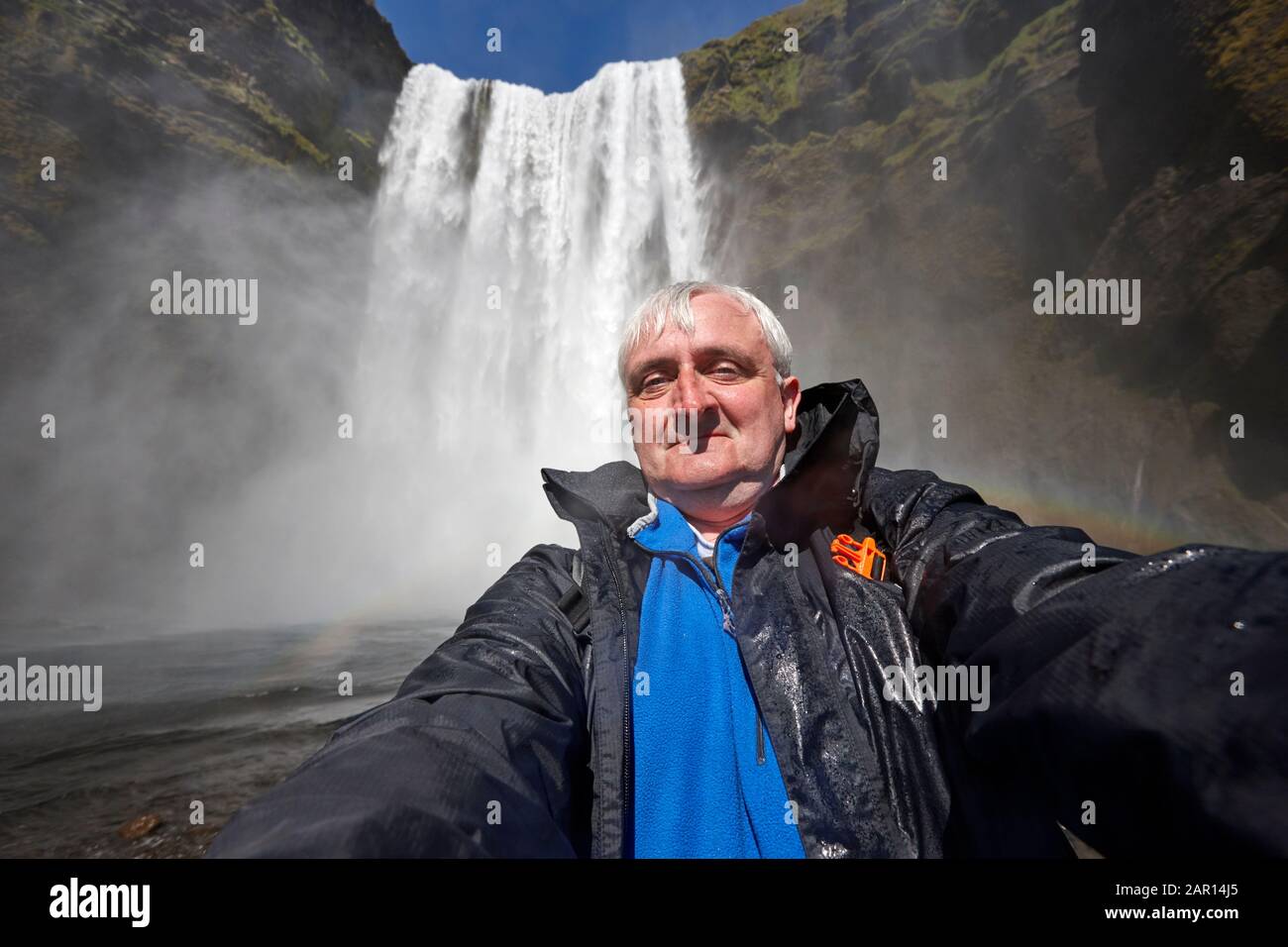 Mitte 40s nimmt grauhaariger alleinstehend männlicher Tourist am skogafoss Wasserfall island ein unbeholfenes Selfie auf Stockfoto