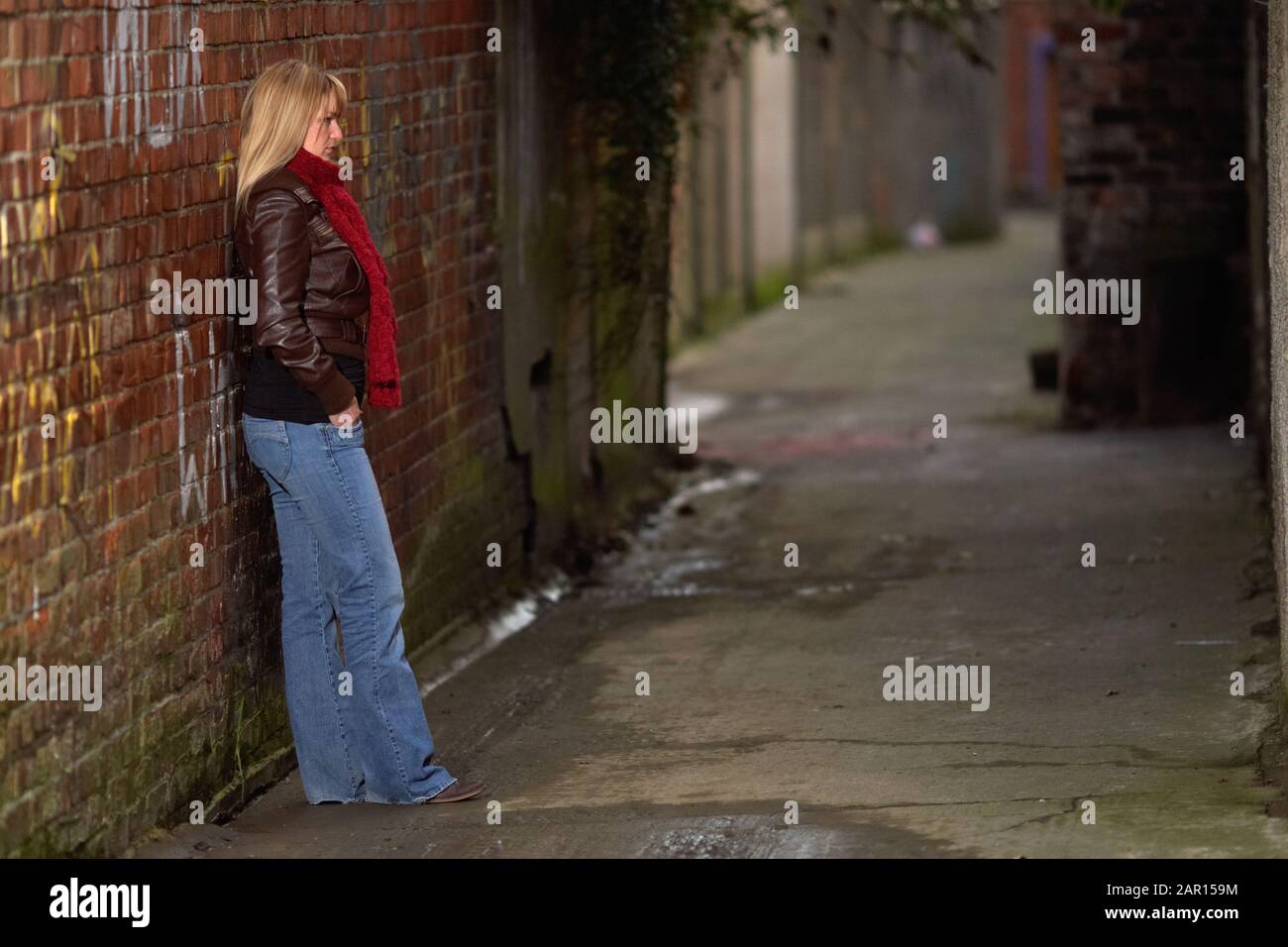 Achtundzwanzig Jahre alte Frau, die sich an einer alten viktorianischen Backsteinmauer in einer Hintergasse im alten Teil von Belfast, Nordirland, lehnt Stockfoto