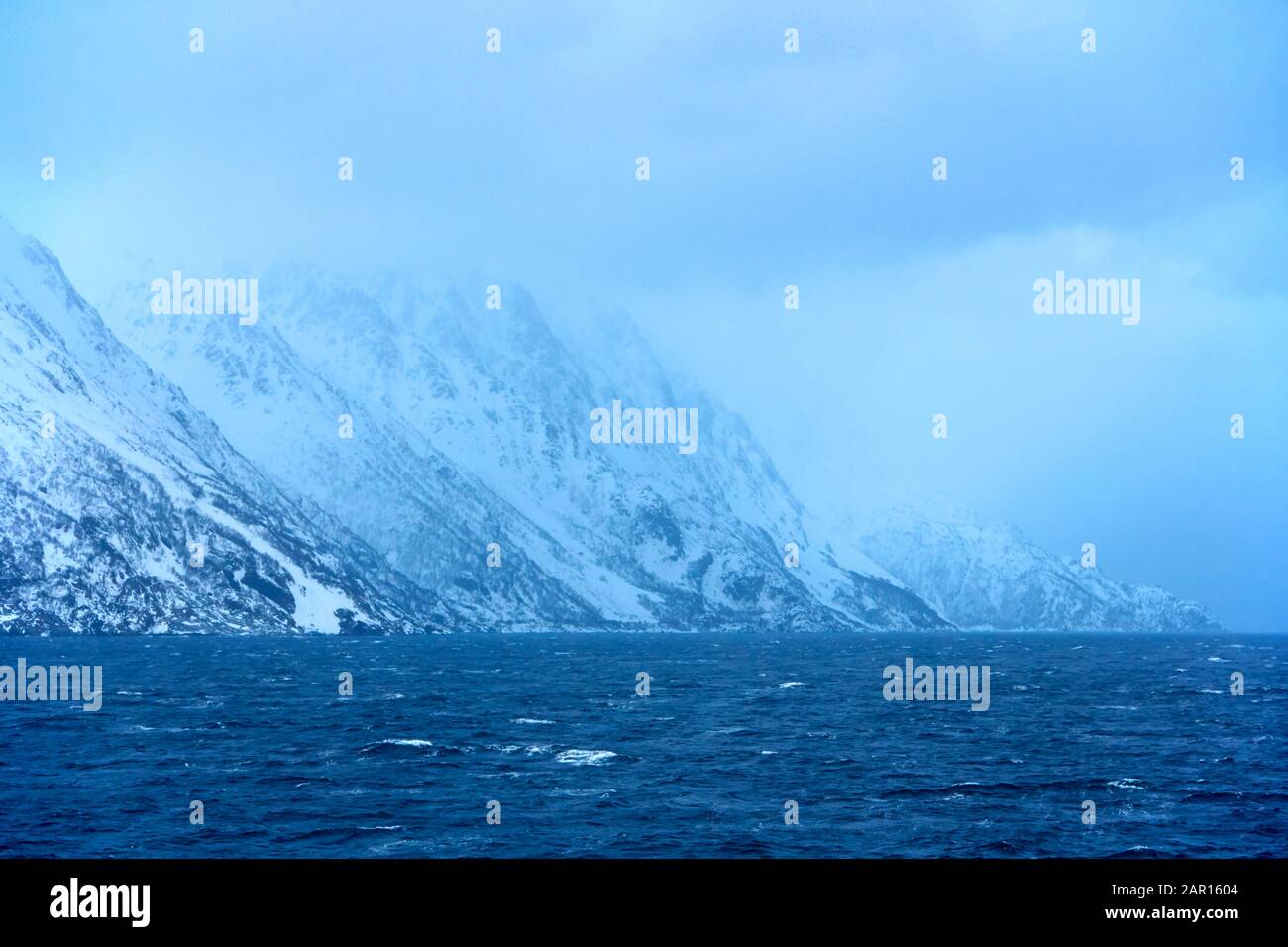 Niedrige Wolke und blaues Winterabendlicht Sonnenlicht auf schneebedeckter arktischer norwegischer Küste Stockfoto