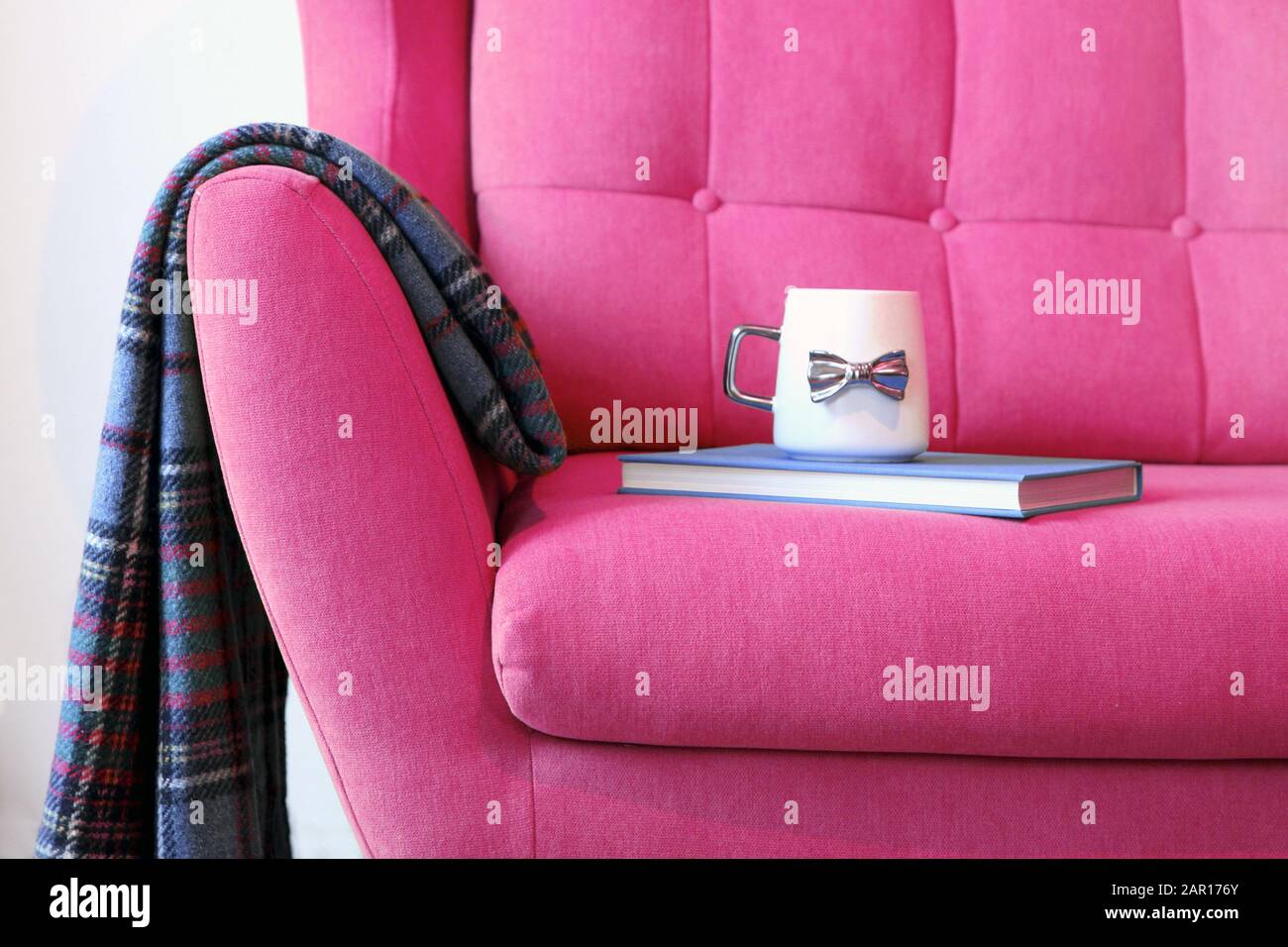 Tasse Tee und blaues Buch auf einem rosafarbenen Trainer mit Decke. Details zum Stillleben im Inneren des Wohnzimmers. Gemütliches Innenleben, Hauskomfort Stockfoto