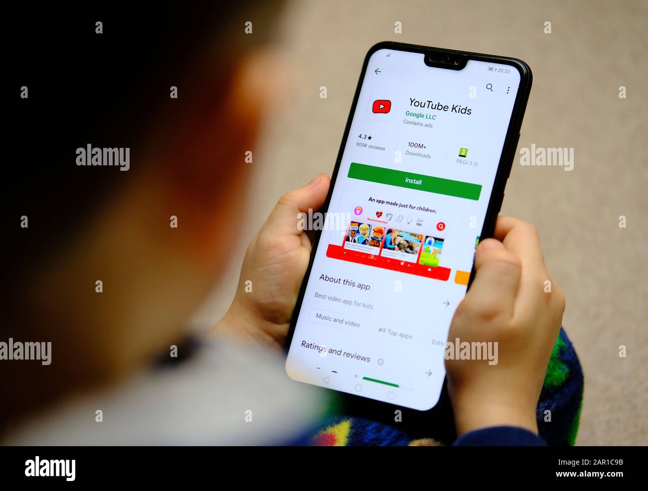 YouTube Kids App im Play Market auf einem Smartphone-Bildschirm und Kind, das es in den Händen hält. Stockfoto