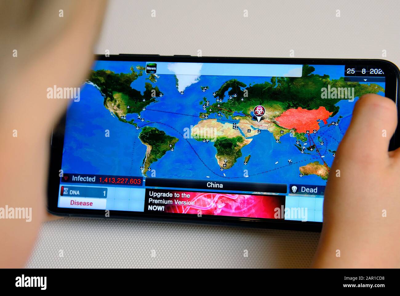 Kind, das auf dem Smartphone das Spiel "Plague Inc." spielt. Strategiesimulationsspiel, das lehrt, wie der Virus verbreitet oder gestoppt werden kann. Konzept. Stockfoto