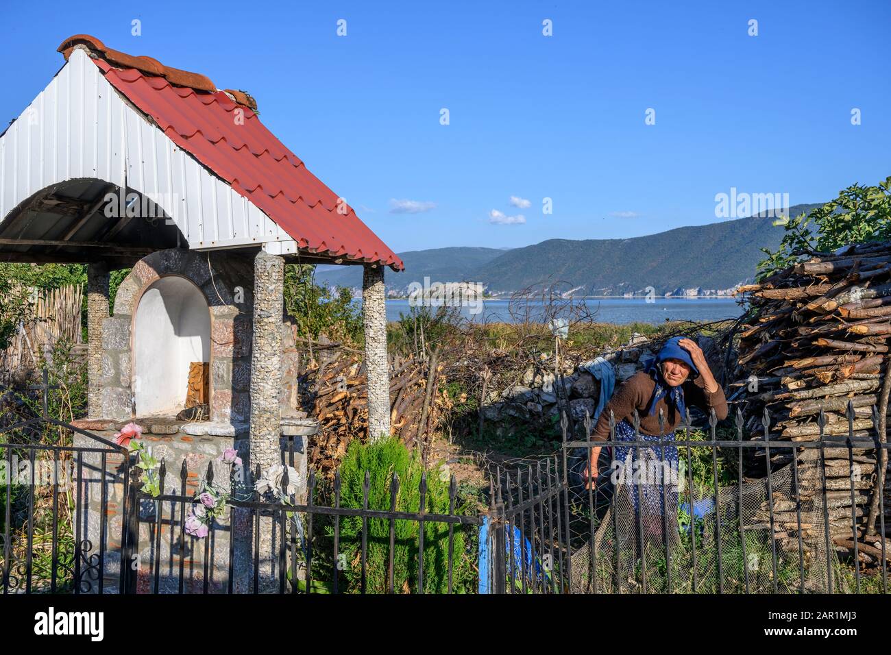 Eine Frau neigt den Garten neben einem Schrein im Dorf Pustec am Ufer des Lake Prespa, Ostalbanien. Stockfoto