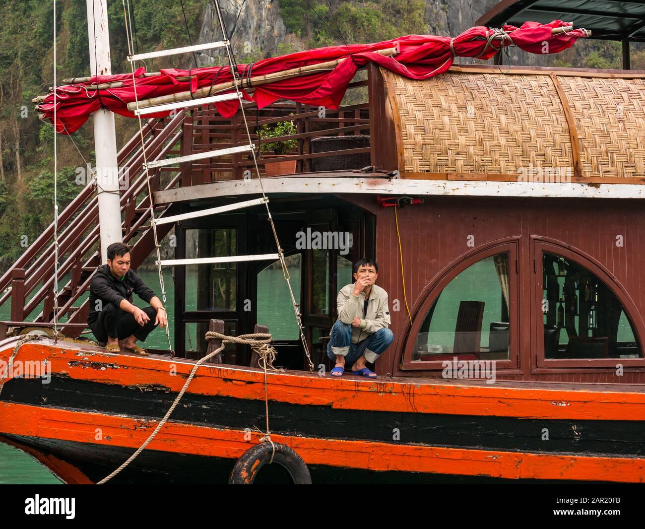 Asiatische Männer, die auf Touristenboot, Cat Ba Island, Lan ha Bay, Vietnam, Asien, hocken und rauchen Stockfoto