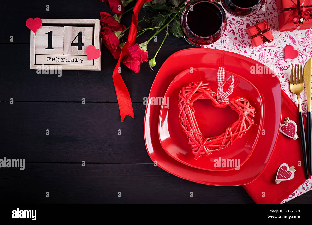 Valentinstag Abendessen mit Tisch mit Geschenk, rote Rosen, Herzen mit zwei Winzerinnen auf dunklem Hintergrund. Draufsicht, flacher Lay. Stockfoto