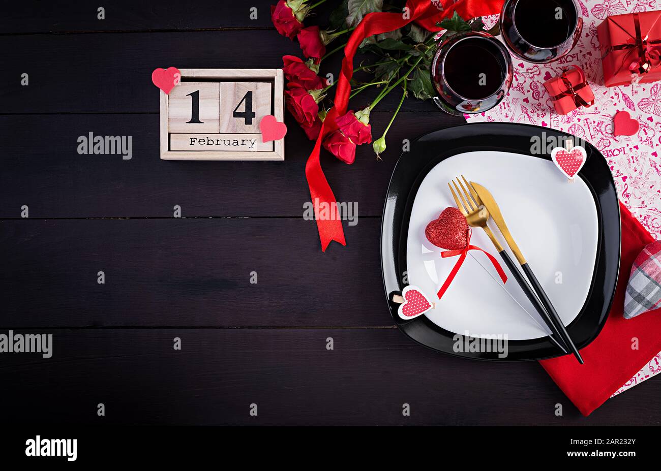 Valentinstag Abendessen mit Tisch mit Geschenk, rote Rosen, Herzen mit zwei Winzerinnen auf dunklem Hintergrund. Draufsicht, flacher Lay. Stockfoto