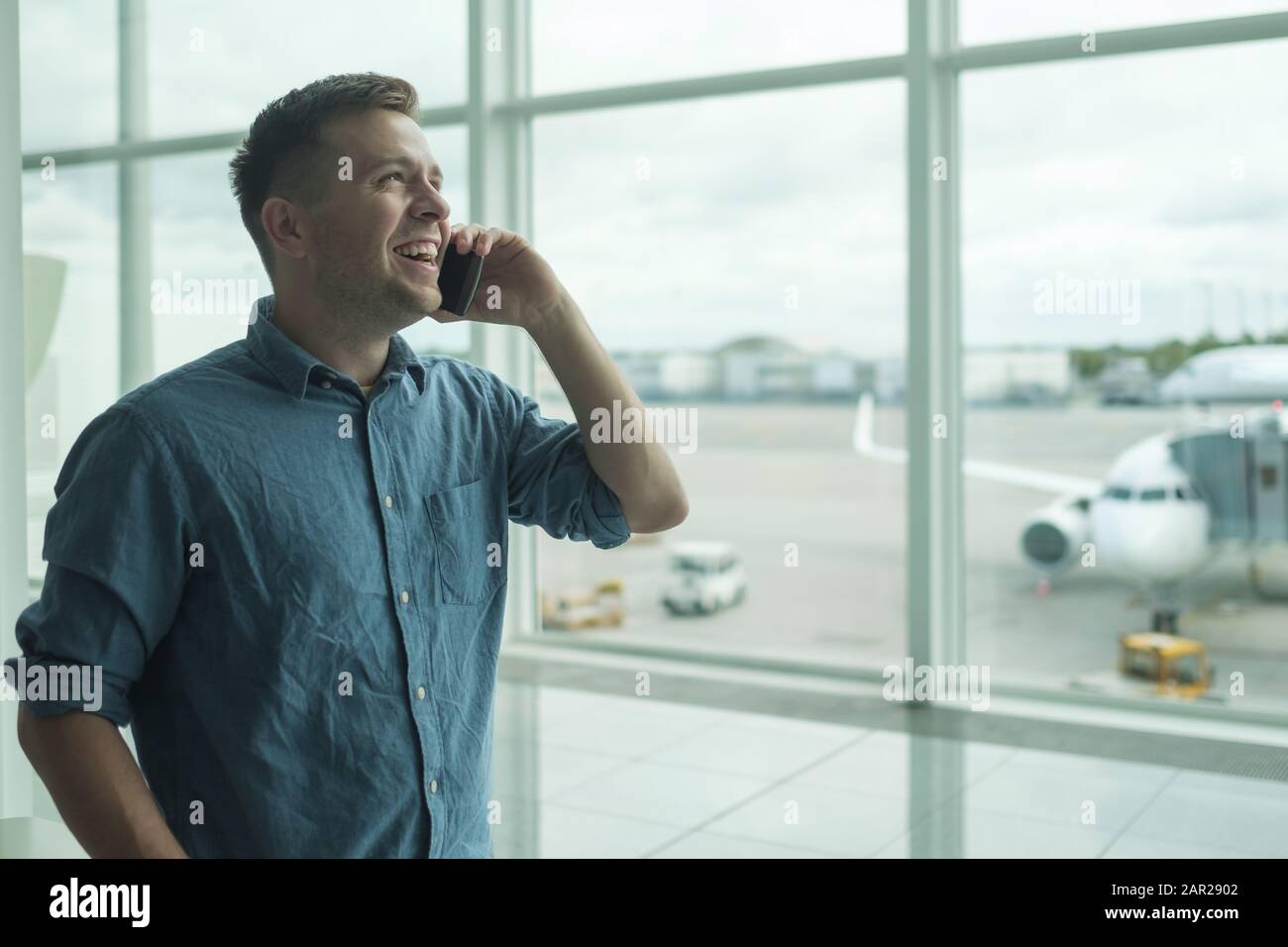 Junger kaukasischer Mann spricht vor dem Flug auf dem Handy am Flughafen Stockfoto