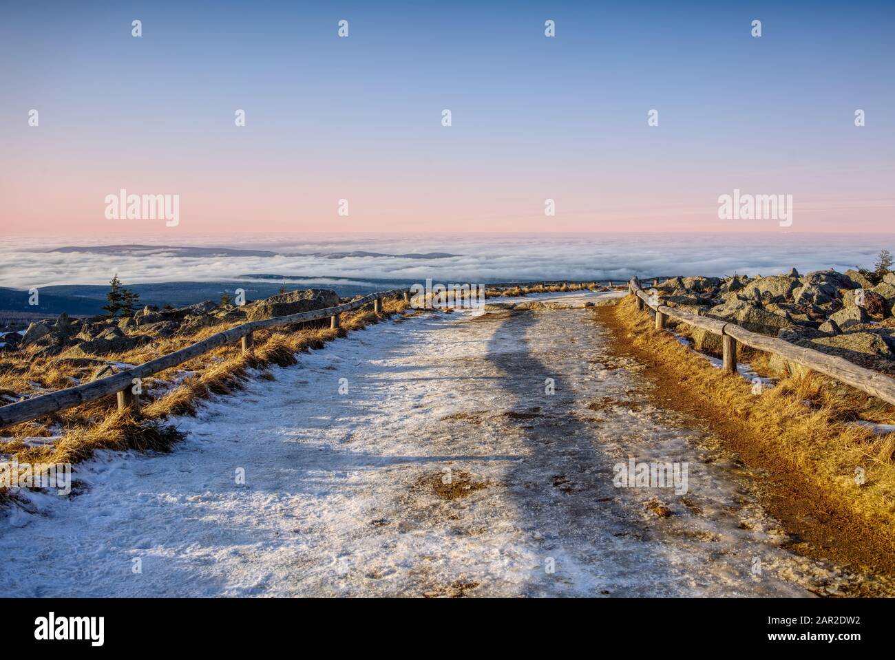 Schneebedeckter Wanderweg über einem Wolkenmeer und einem Himmel in Pastelle. Romantische Winterlandschaft auf dem Brocken, Harz, Deutschland. Stockfoto