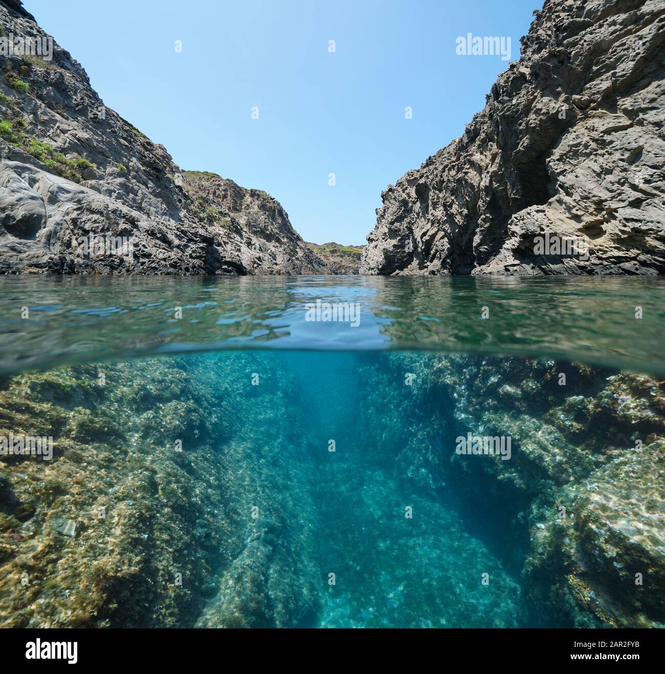 Mediterrane Felsküste mit einer Passage zwischen Felsen, geteiltem Blick über und unter der Wasseroberfläche, Spanien, Costa Brava, Katalonien, Cap de Creus Stockfoto